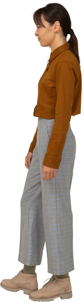 Vista lateral de uma jovem mulher asiática com uma careta zangada de calça e blusa