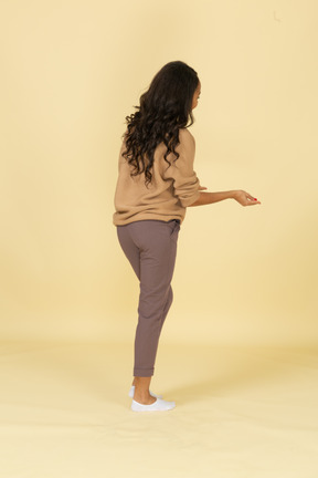 Three-quarter back view of a dark-skinned smiling young female outstretching her hands