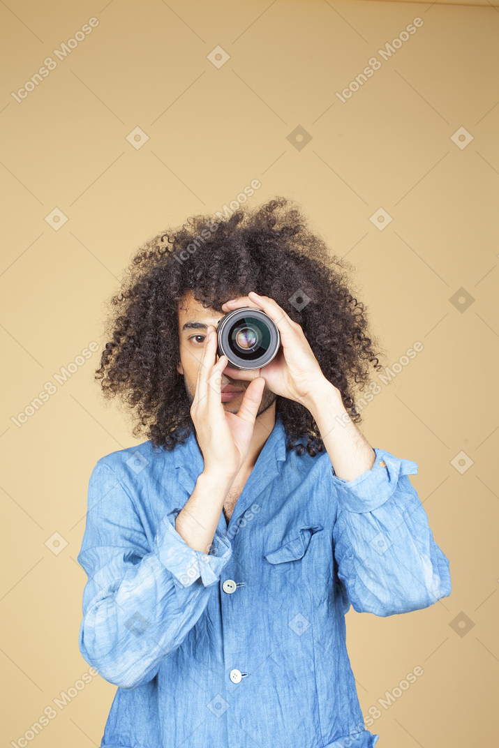 Man in denim suit holding a camera next to his face