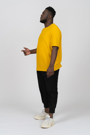 Three-quarter view of a thoughtful young dark-skinned man in yellow t-shirt raising hand