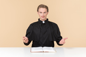 Catholic priest sitting at the table with open bible book on it