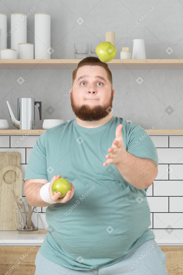 A man juggling apples in kitchen