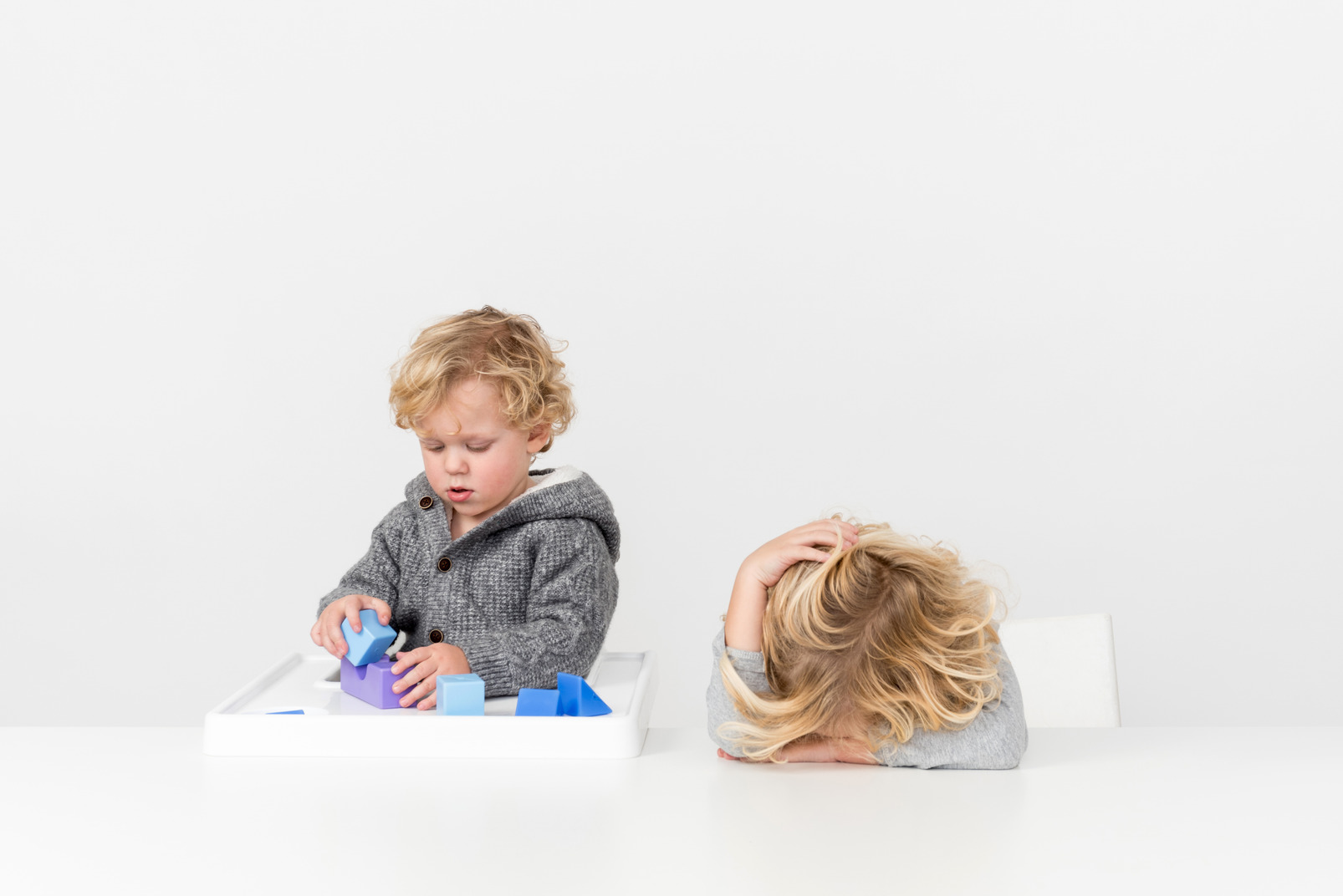 Baby boy playing with cubes and kid boy lying on the table