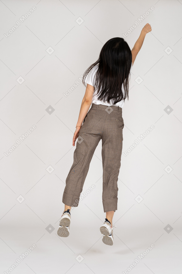 Vista posteriore di una giovane donna che salta in calzoni e t-shirt protese la mano