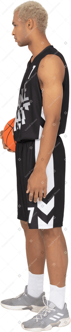 Vista laterale di un giovane giocatore di basket maschile che tiene una palla