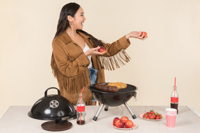 Jeune femme asiatique tenant des fruits et debout près de grill