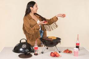 Joven mujer asiática con frutas y de pie junto a la parrilla