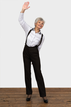 Front view of an old female in office clothes making a greeting gesture raising her hand