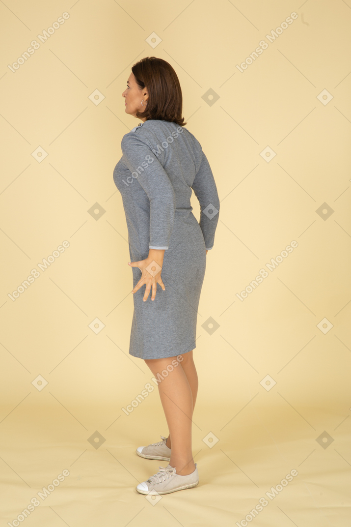 Женщина в сером платье стоит в профиль