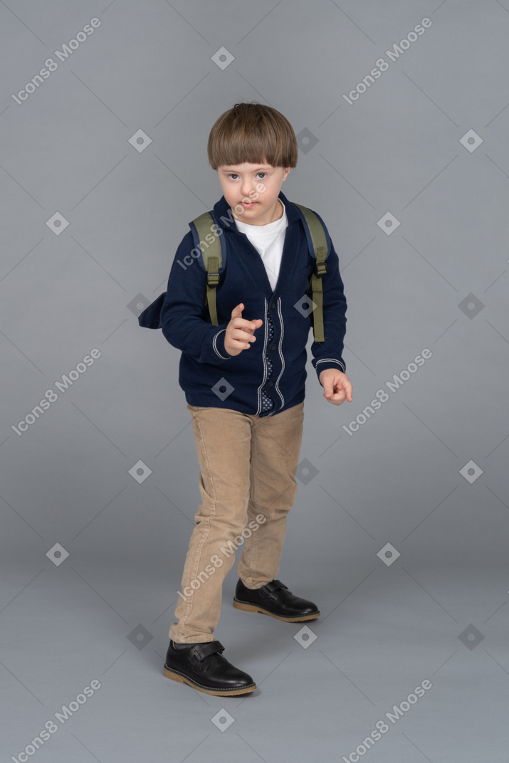 Portrait of a little boy with a backpack holding up a hand