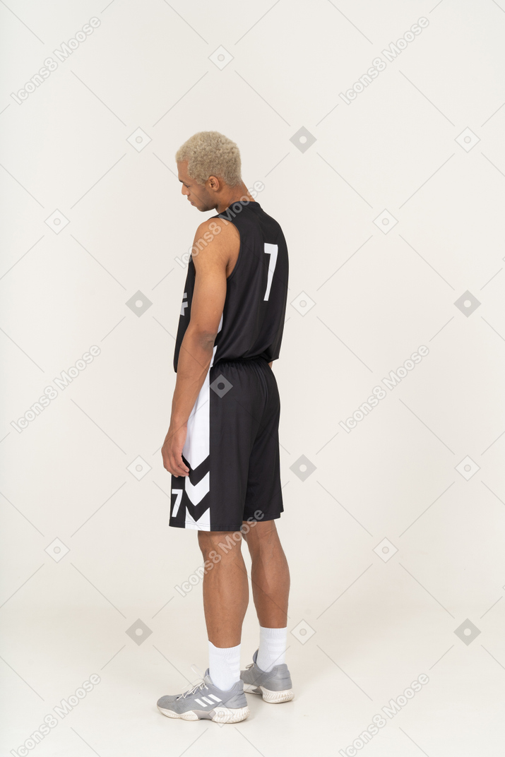一个疲惫的年轻男篮球运动员倾斜头部的四分之三后视图