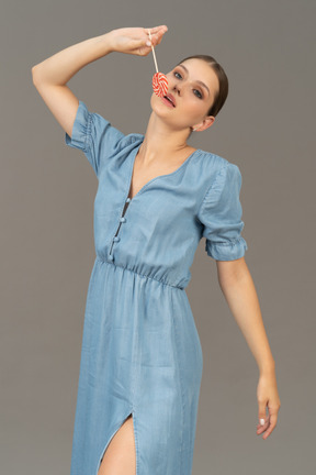 Three-quarter view of a young woman in blue dress holding a lollipop