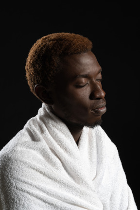 Side shot of a man sitting peacefully wrapped in a towel with his eyes closed