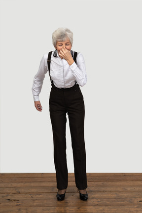 Vista frontal de uma mulher idosa com roupas de escritório espirrando dentro de casa