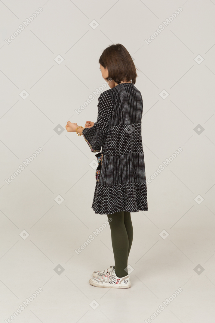 Vista posterior de tres cuartos de una niña furiosa en vestido apretando los puños