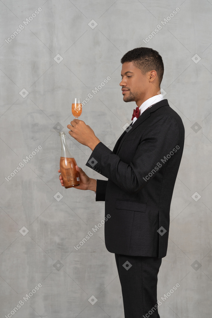 Mann, der eine schnapsflasche hält und ein flötenglas betrachtet