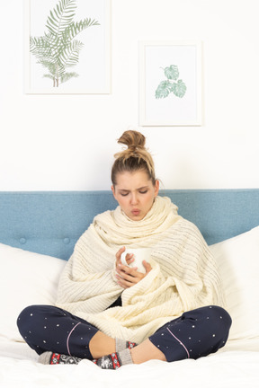 Front view of an ill young lady wrapped in white blanket staying in bed