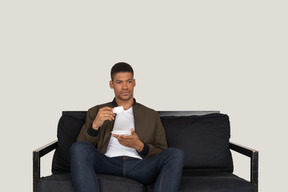 Front view of a young dreaming man sitting on a sofa with a cup of coffee