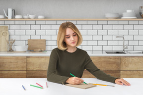 A woman sitting at a table with a notebook and pencils