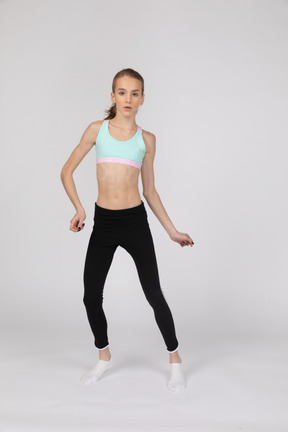 Vista frontal de una jovencita en ropa deportiva bailando mientras mira a la cámara