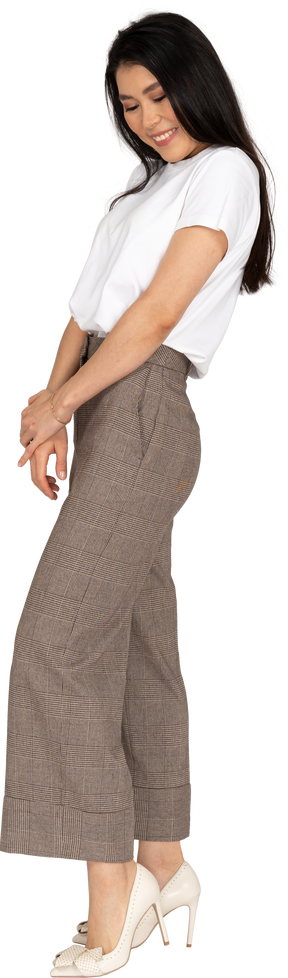 Vista lateral de una tímida señorita sonriente en calzones y camiseta tomados de la mano juntos