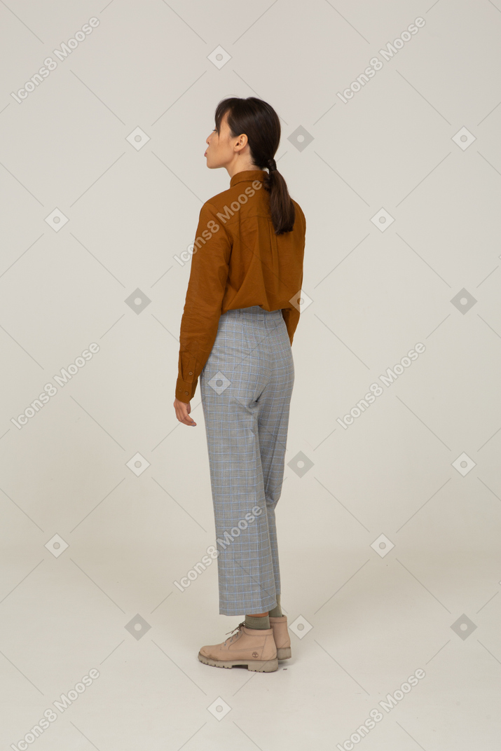 Vista posteriore di tre quarti di una giovane donna asiatica imbronciata in calzoni e camicetta
