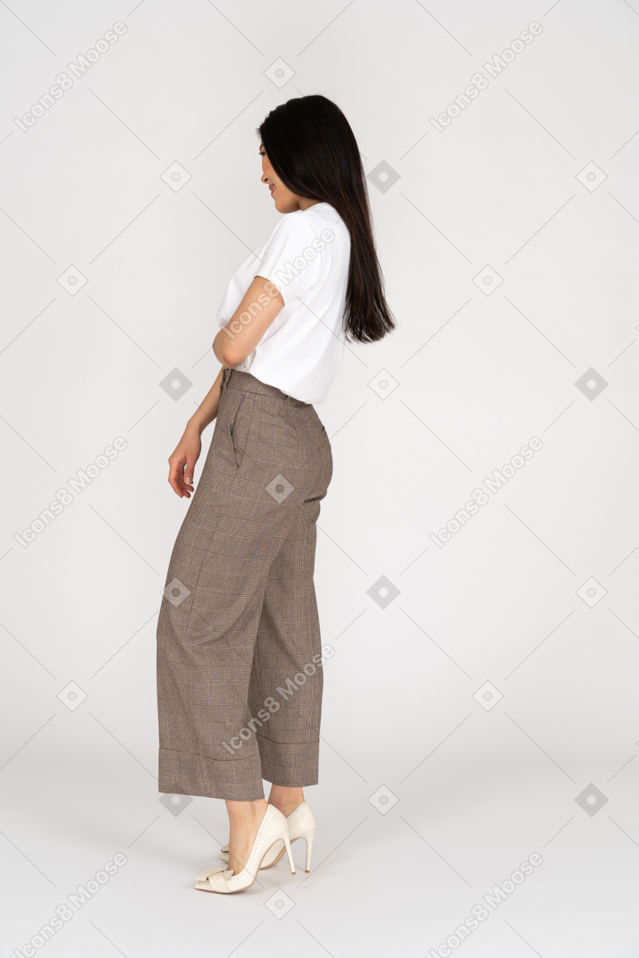 Vista lateral de uma jovem sorridente e tímida de calça e camiseta
