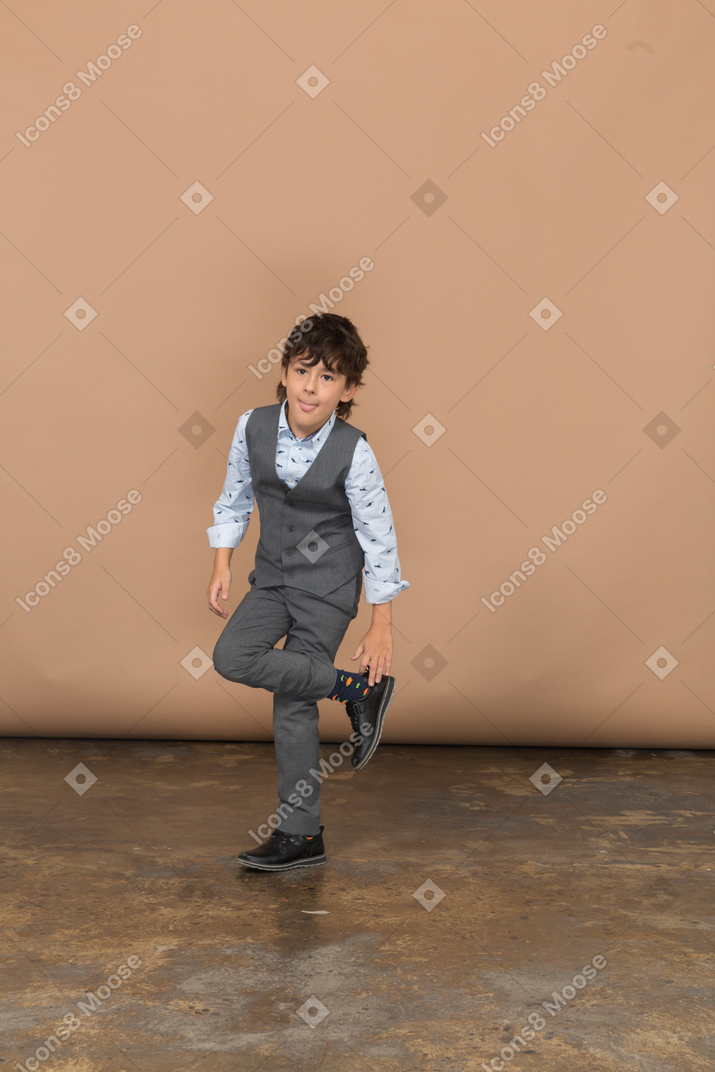 一个穿着灰色西装的男孩交叉双腿站立的正面图
