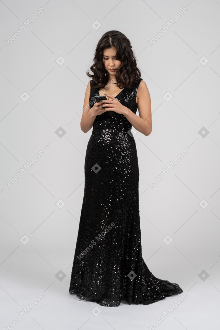 Женщина в черном вечернем платье проверяет телефон