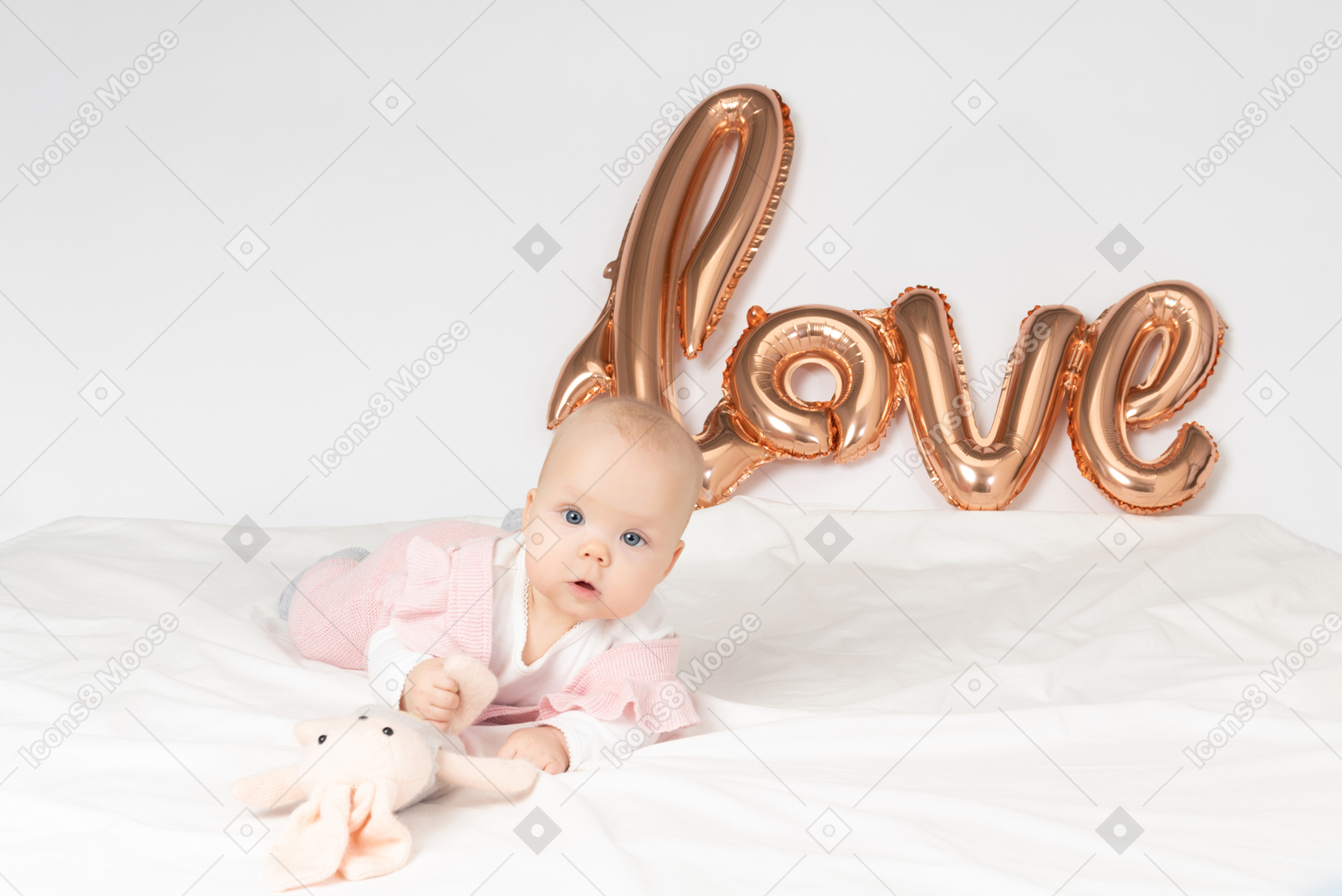 Baby girl lying on the stomach with stuffed toy and balloon love sign back on the wall