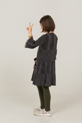 Three-quarter back view of a little girl in dress showing peace sign