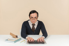 Joven estudiante asiática en un suéter escribiendo en una computadora portátil