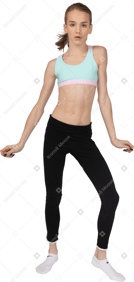 Vista frontal de uma adolescente em roupas esportivas dançando enquanto olha para a câmera
