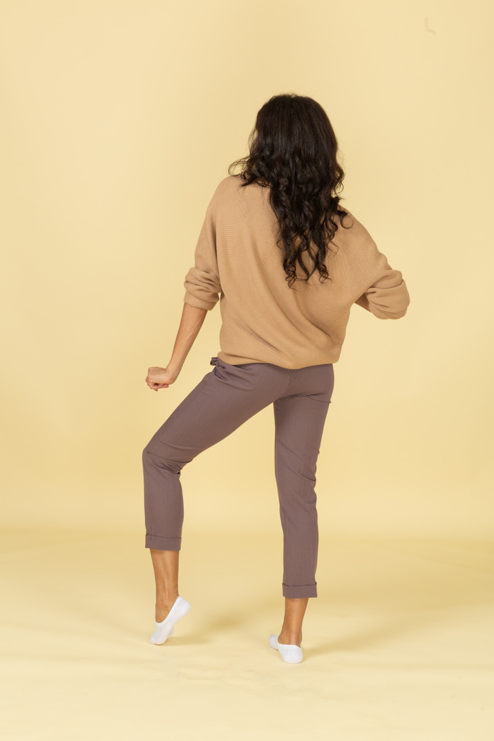 Back view of a dancing dark-skinned young female bending knee