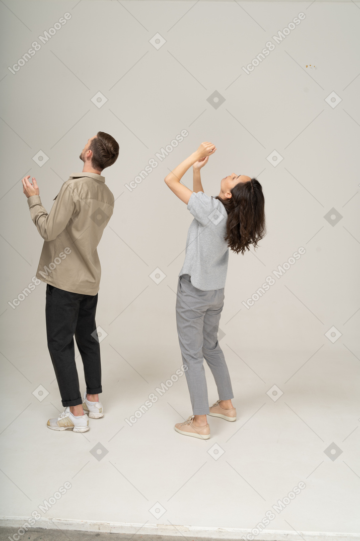 Homem e mulher olhando para cima e levantando as mãos