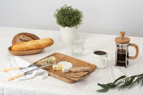 Cheese and bread on the tray next to french press and cup of coffee