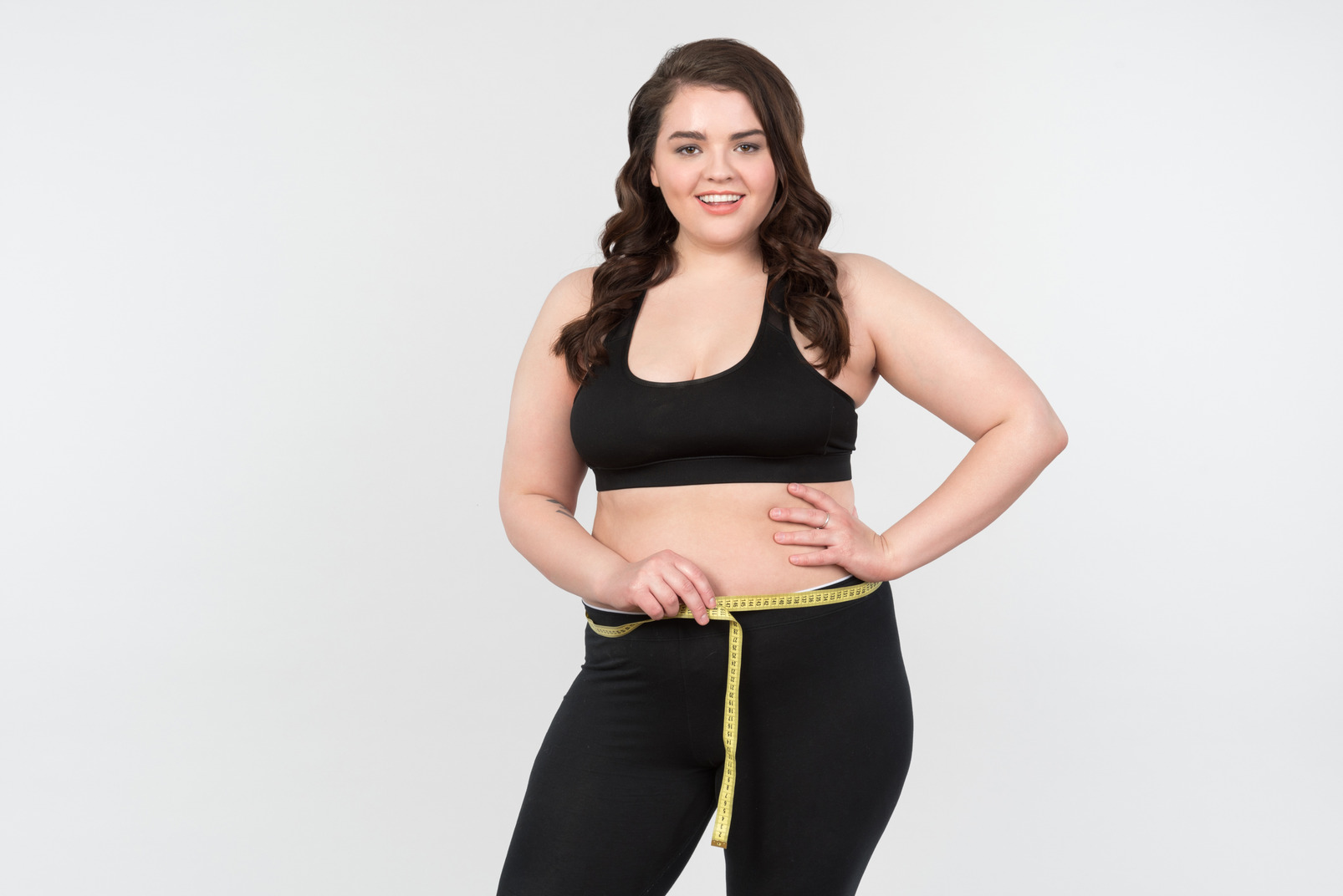 Smiling young plus-size model measuring her waist