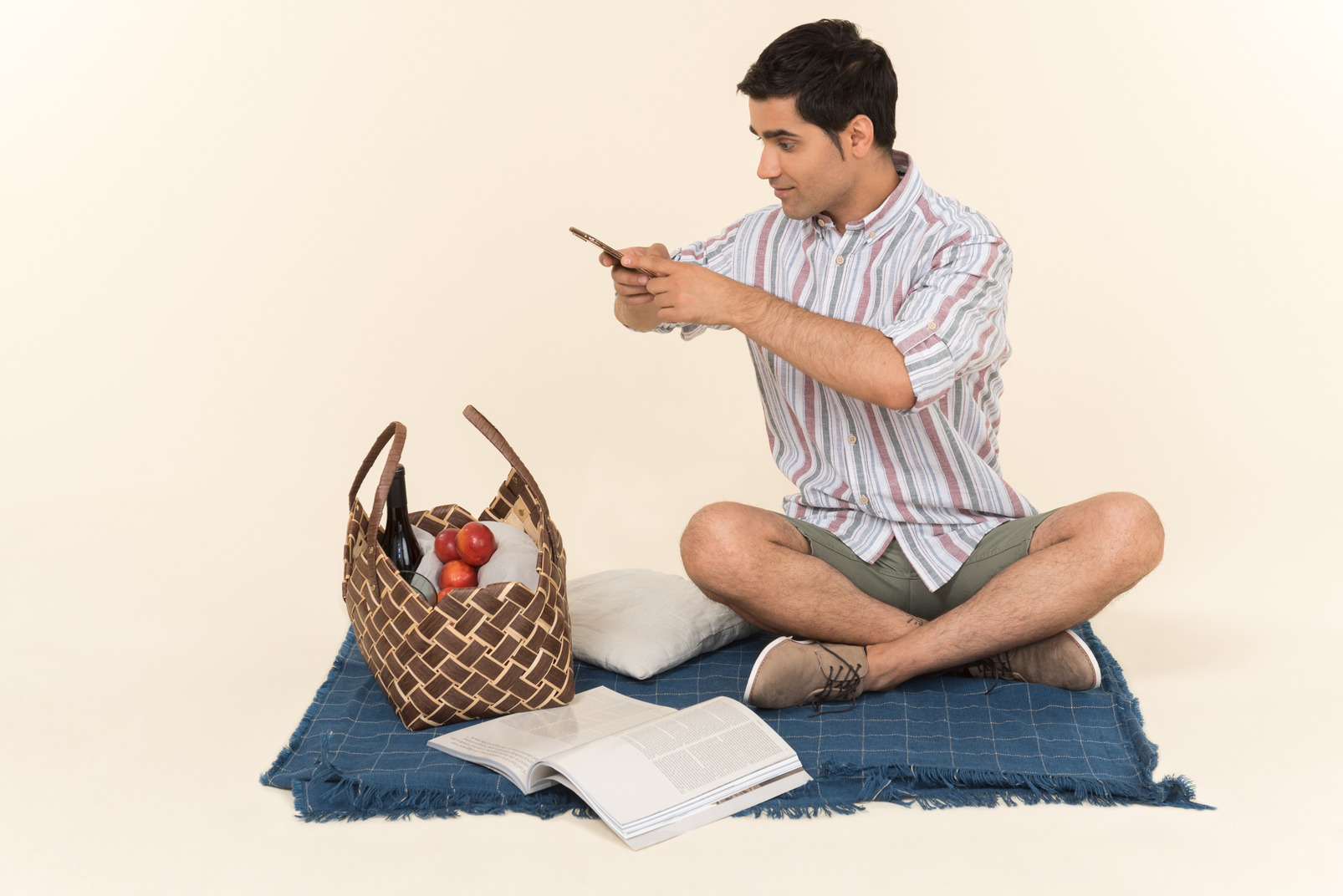 Young caucasian guy sitting on blanket and making a photo of picnic basket