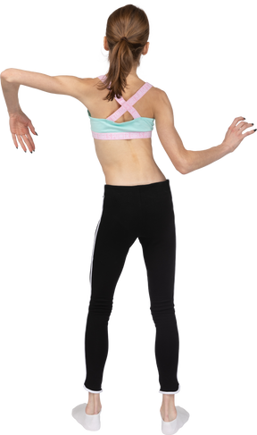 Vista posterior de una jovencita en ropa deportiva inclinando los hombros y haciendo olas