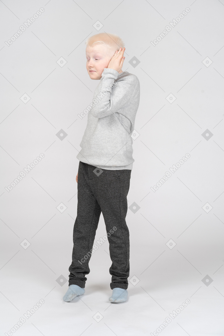Vista de tres cuartos de un niño poniendo la palma de la mano en la oreja