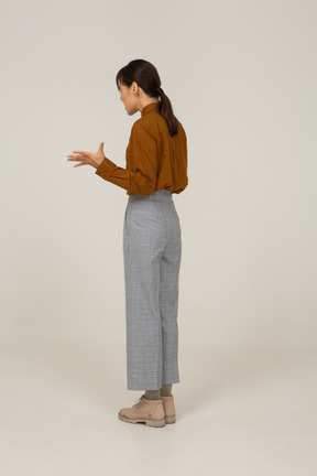 Vista posteriore di tre quarti di una giovane donna asiatica gesticolante in calzoni e camicetta