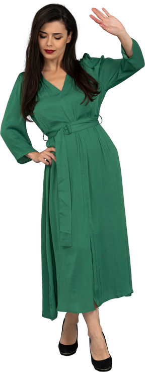 Vue de face d'une jeune femme en robe verte mettant la main sur la hanche tout en levant la main
