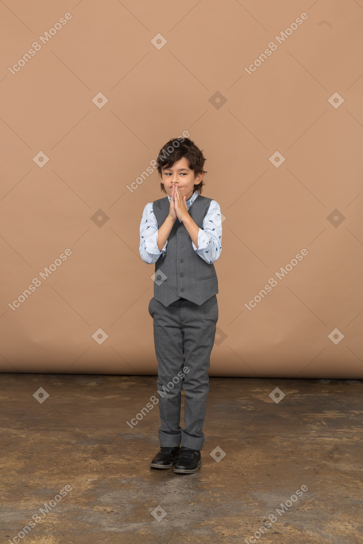 Vista frontal de un niño con traje gris haciendo un gesto de oración