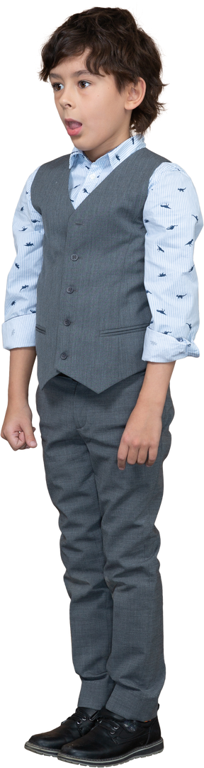 Vista frontal de un chico lindo en traje gris de pie con la boca abierta