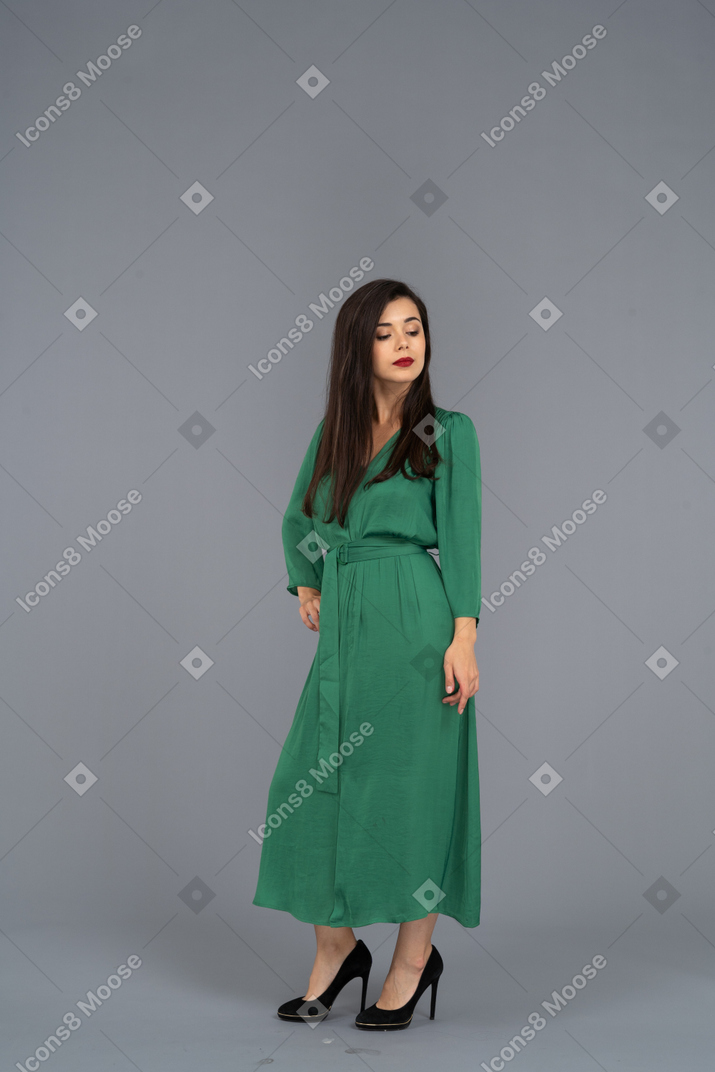 腰に手を置いている緑のドレスを着た誇り高き若い女性の4分の3のビュー