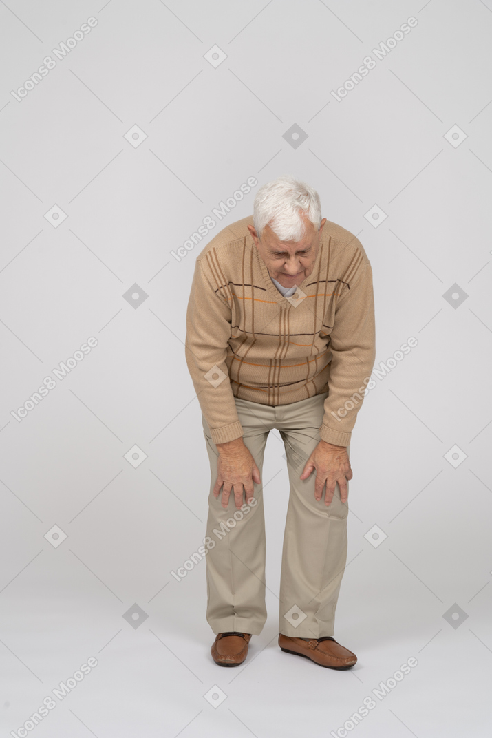 Vista frontal de un anciano agachándose y tocándose las rodillas doloridas