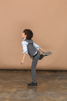 Side view of a boy in grey suit posing on one leg