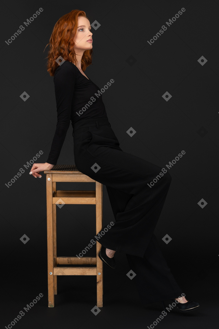 A side view of the sexy woman sitting on the wooden chair and looking to the right side