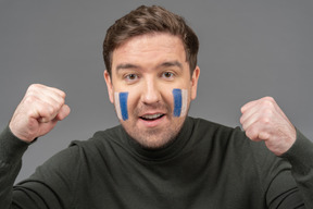 Vue de face d'un fan de football masculin avec art visage bleu et blanc poing serrant