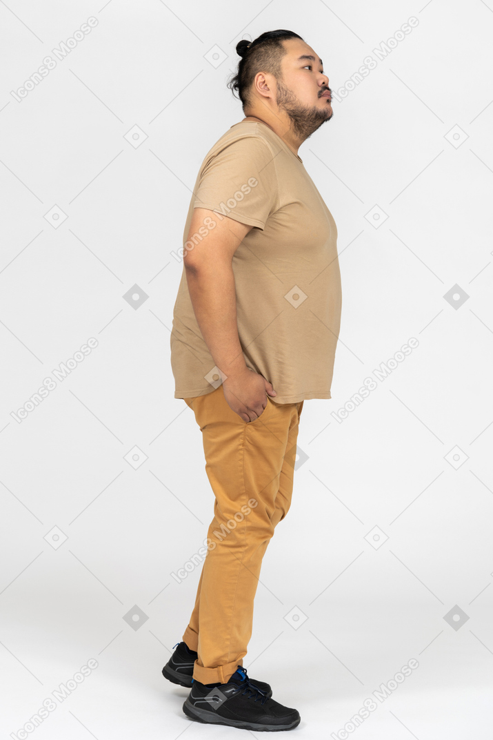 Thoughtful asian man standing in profile with hands in pockets